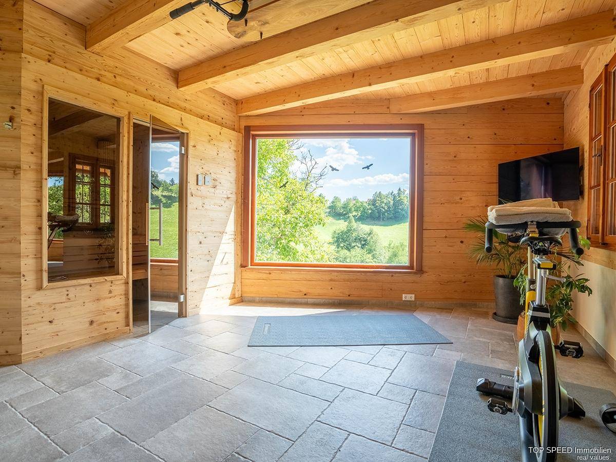 Heller Fitnessraum mit Holzwänden, Fliesenboden und großem Fenster mit Blick auf die grüne Landschaft.