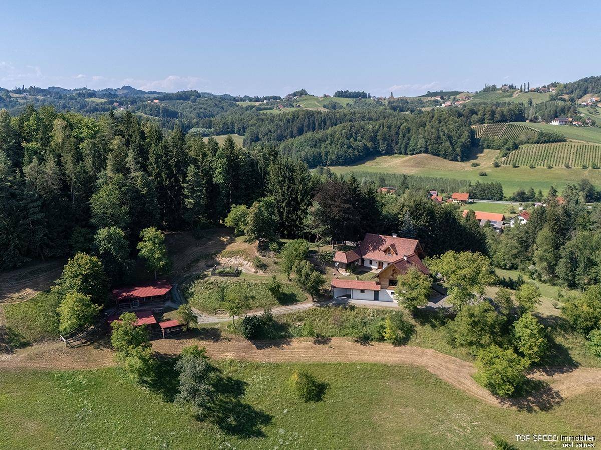 Luftaufnahme eines Anwesens mit mehreren Gebäuden, umgeben von Wäldern und Weinbergen in hügeliger Landschaft.