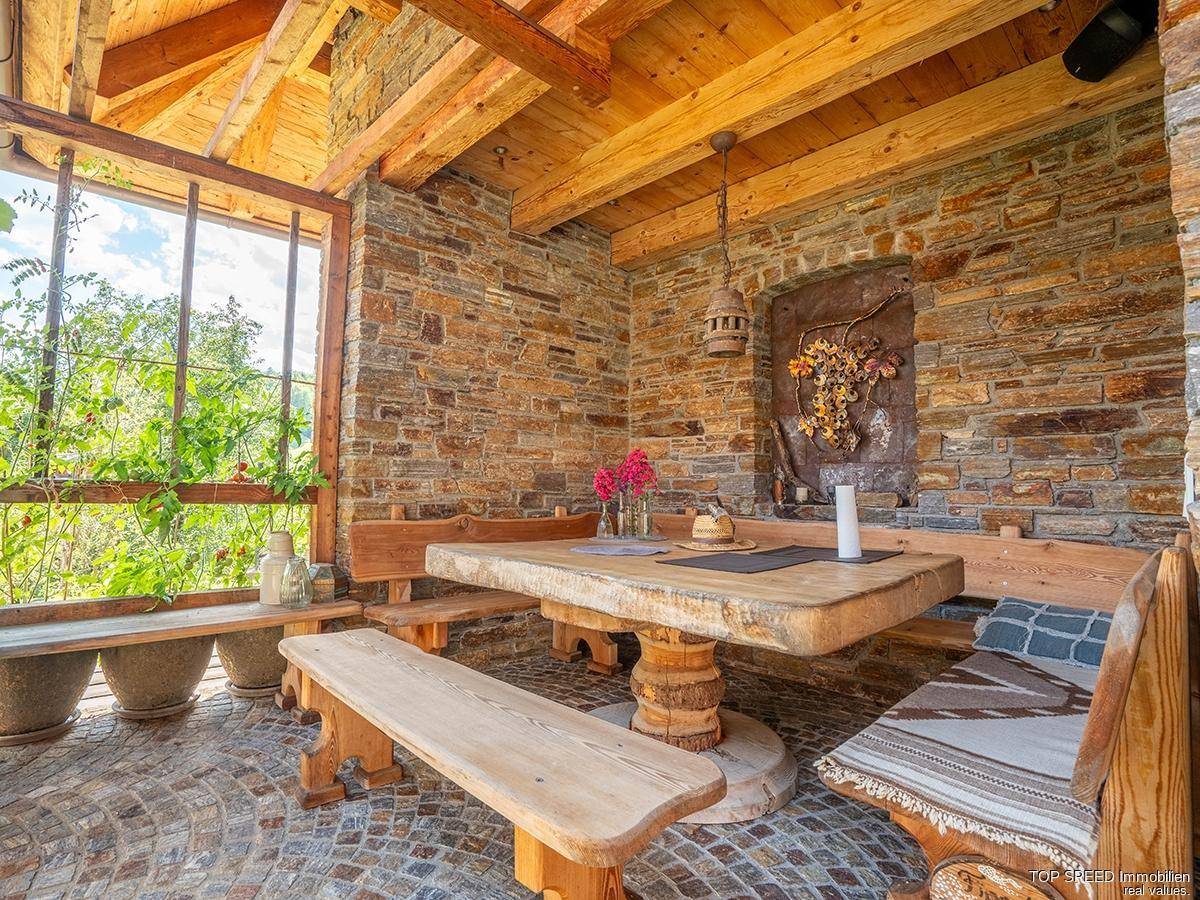 Rustikaler Essbereich im Freien mit Holztisch und Bänken, umgeben von Steinmauern und Holzbalken.