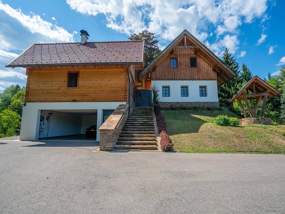 Traditionelles Holzhaus mit Steintreppe, integrierter Garage und weitläufiger Auffahrt in ländlicher Umgebung.