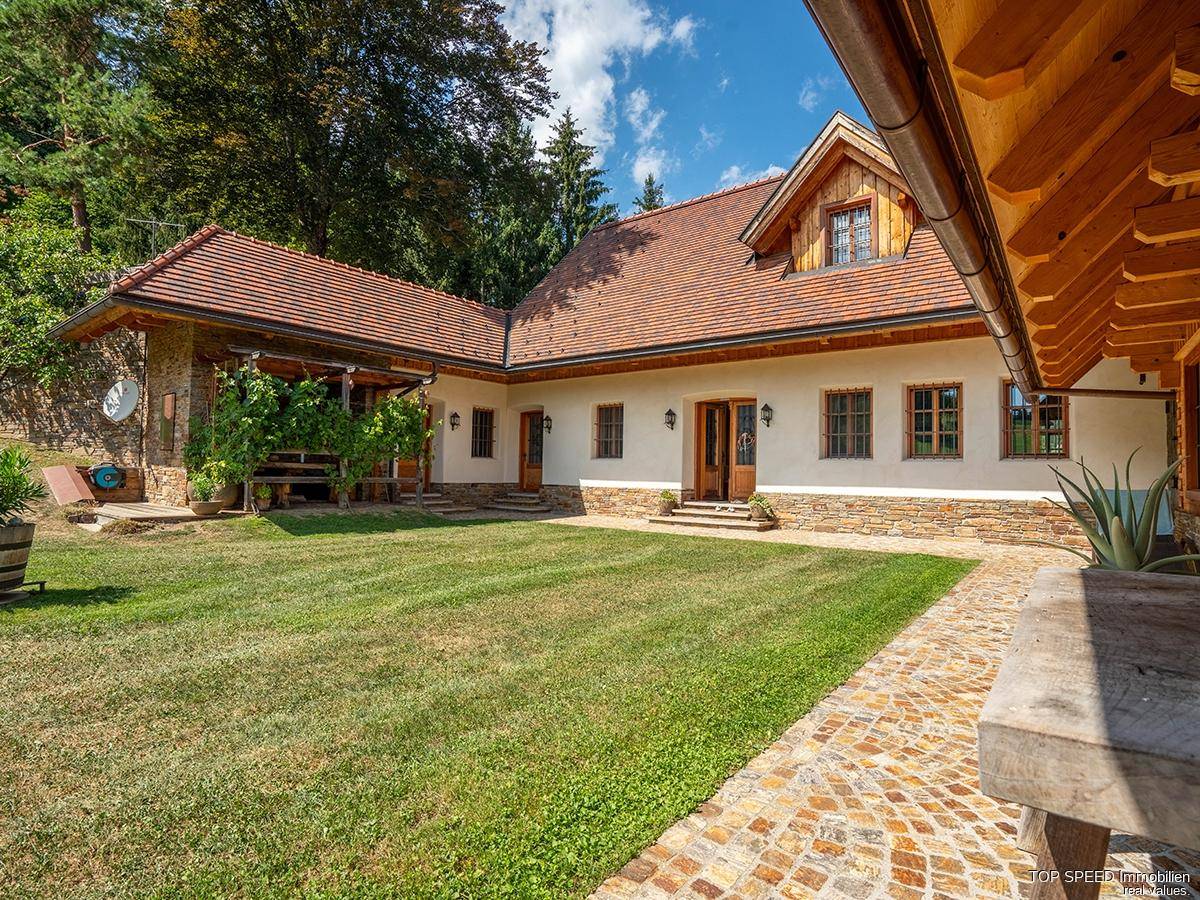 Gepflegter Rasenbereich mit Steinweg vor einem traditionellen Haus mit Holzelementen und überdachtem Eingangsbereich.