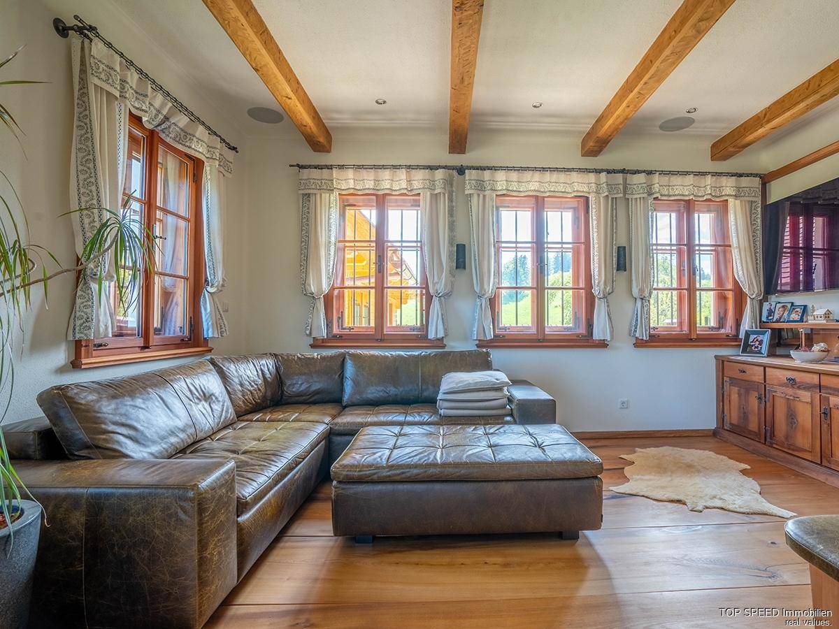 Gemütliches Wohnzimmer mit Ledersofa, Holzboden und sichtbaren Deckenbalken, hell und einladend.