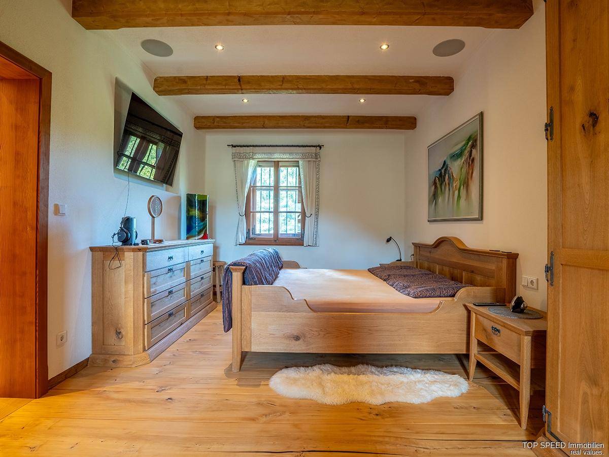 Gemütliches Schlafzimmer mit Holzbett, Holzboden und sichtbaren Deckenbalken, hell und einladend.