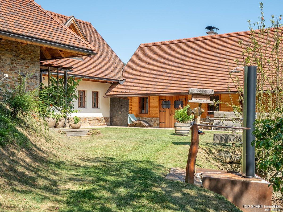 Gepflegter Gartenbereich mit Rasen und Außenkamin vor einem traditionellen Holzhaus mit Steinelementen.