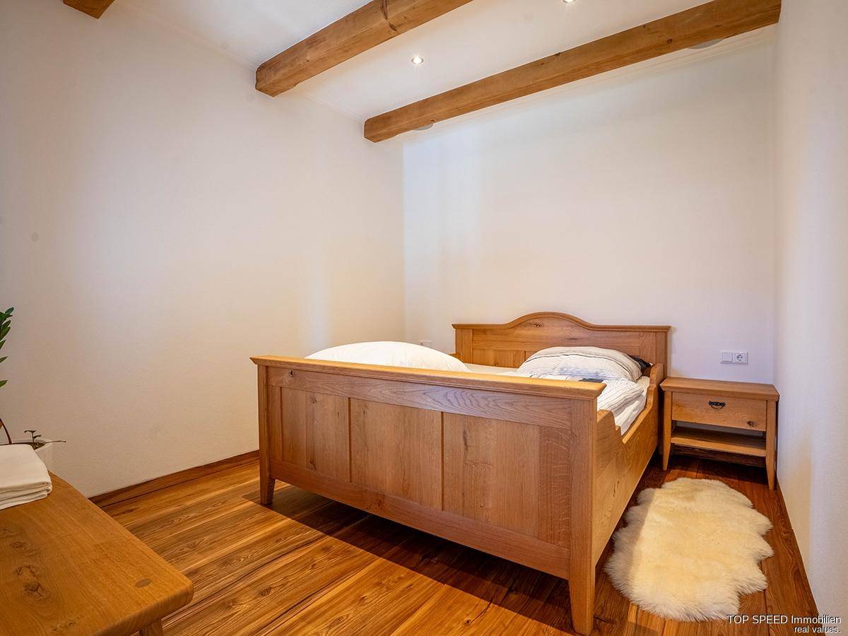Helles Schlafzimmer mit Holzbett, Holzboden und schlichten weißen Wänden, ruhig und komfortabel.