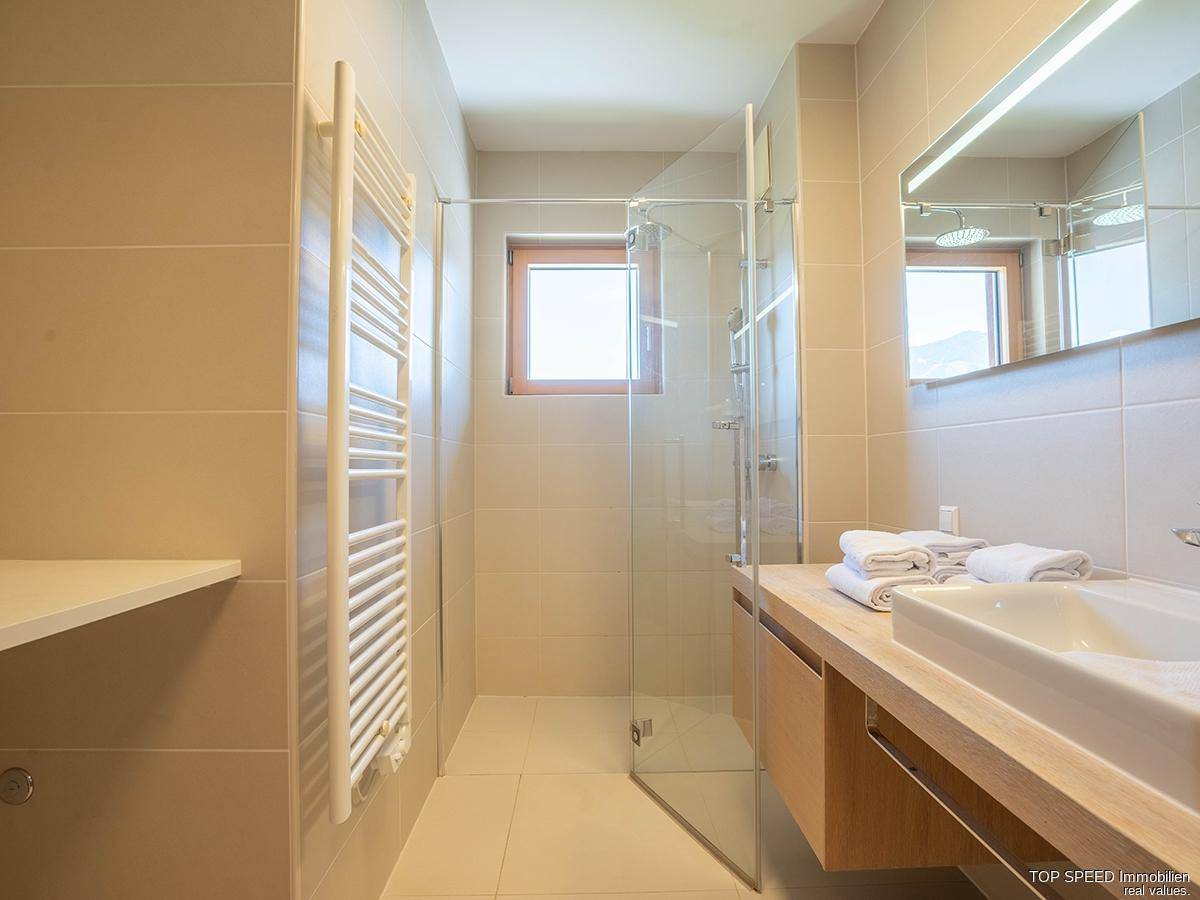 Modernes Badezimmer mit ebenerdiger Dusche, Einzelwaschbecken, beheiztem Handtuchhalter und Fenster.