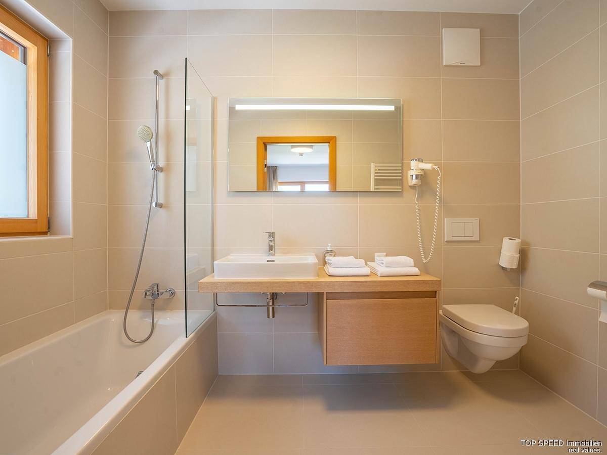 Helles Badezimmer mit Badewanne, Einzelwaschbecken, wandhängendem WC und einem Fenster für Tageslicht.