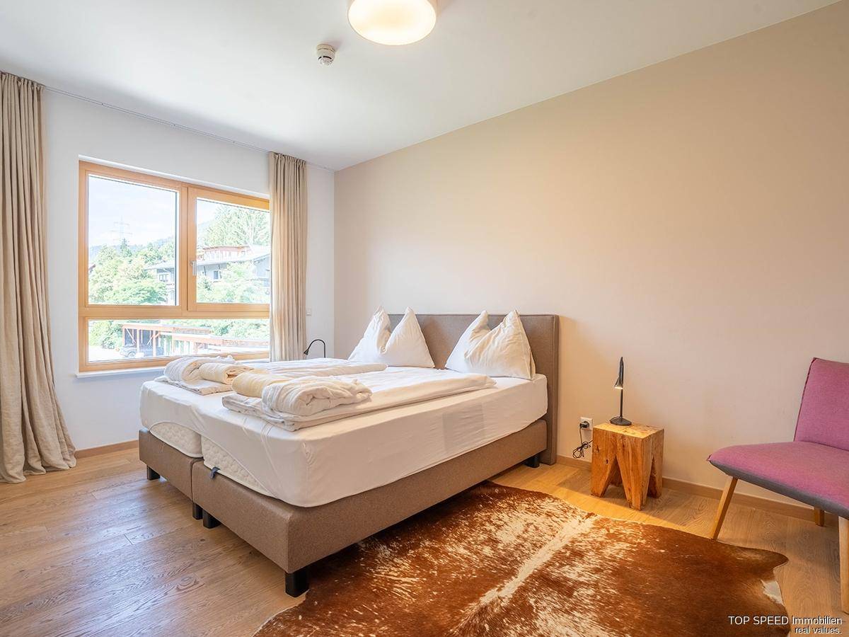 Gemütliches Schlafzimmer mit Doppelbett, Holzboden und einem großen Fenster mit Blick ins Grüne.