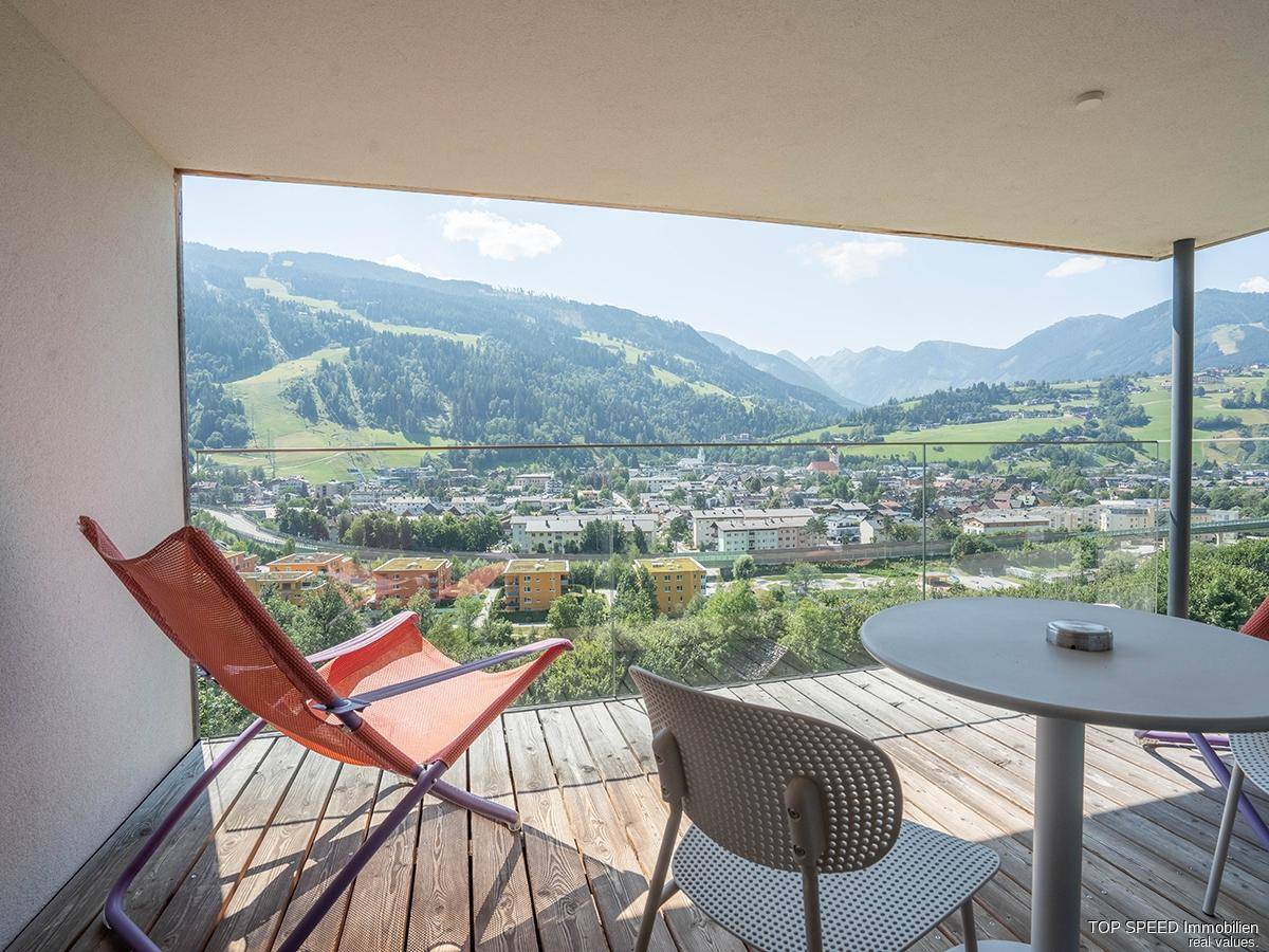 Großer Balkon mit Glasgeländer und Sitzgelegenheiten, bietet eine atemberaubende Aussicht auf die Berglandschaft.