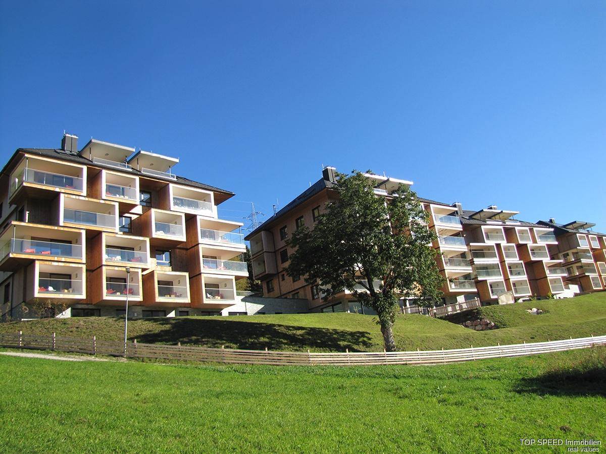 Moderne Apartmentgebäude in Hanglage mit ansprechender Architektur und grüner Umgebung unter blauem Himmel.