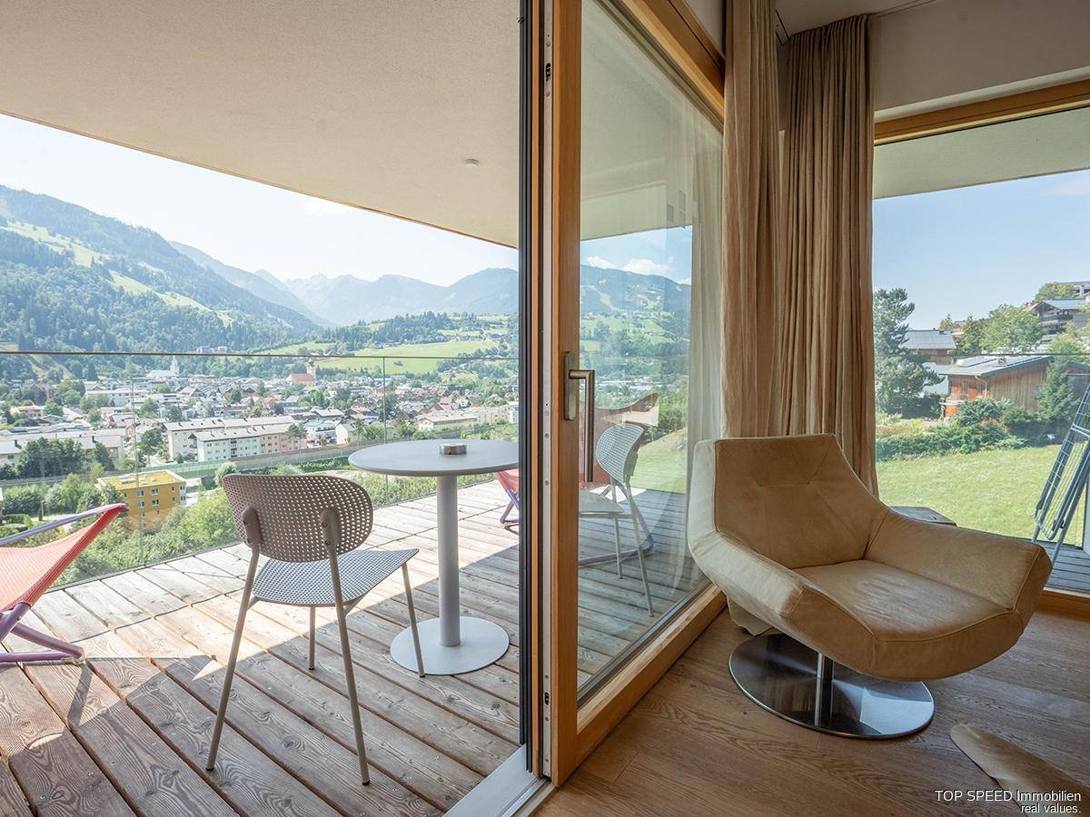 Geräumiger Balkon mit Holzboden und Sitzgelegenheiten, bietet einen weiten Blick auf die Berge und das Tal.