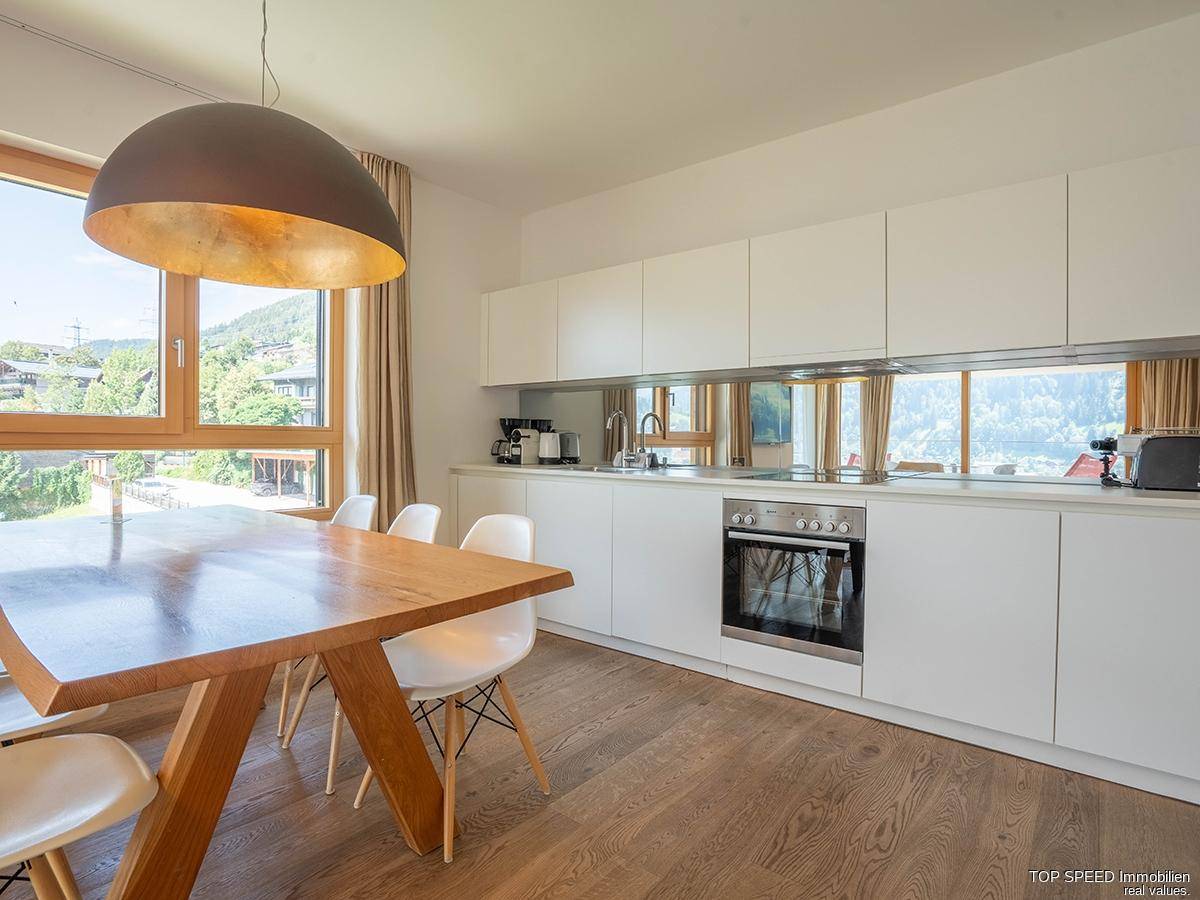 Moderne Küche mit weißen Schränken, integriertem Backofen und einem Esstisch mit Bergblick.