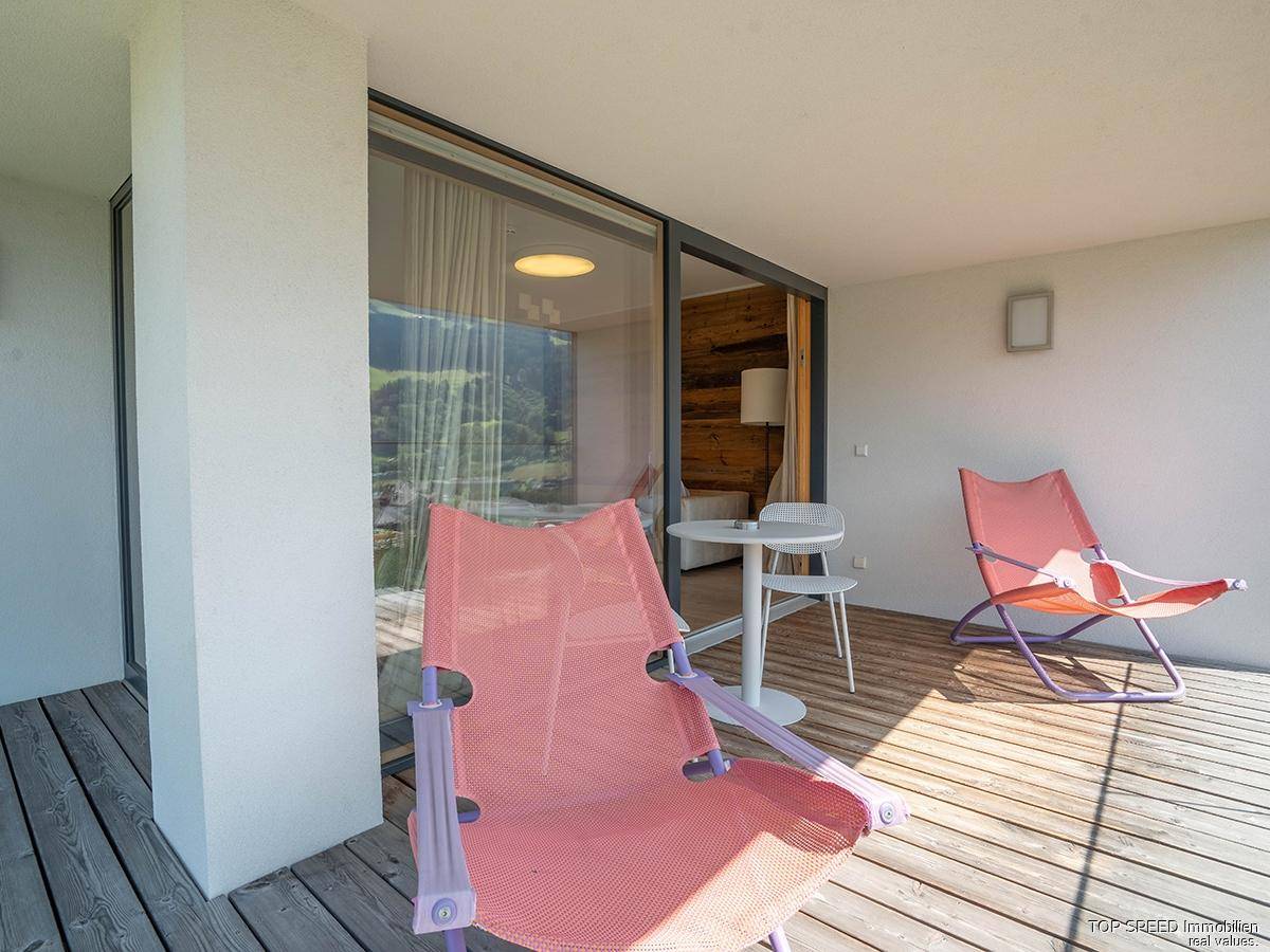 Sonniger Balkon mit Holzdeck und bequemen Stühlen, direkt zugänglich vom Wohnbereich durch große Schiebetüren.