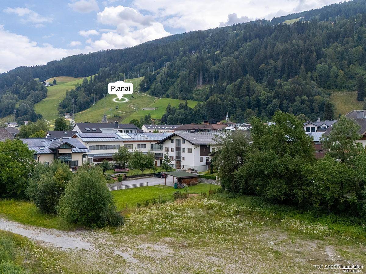 Weitläufiger Blick auf die Bergwelt mit dem Ort Planai und bewaldeten Hängen im Hintergrund.