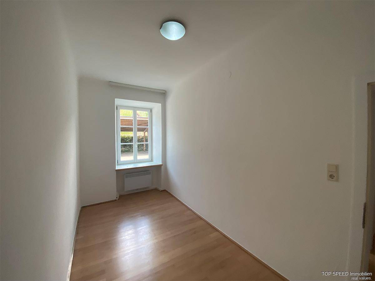 Kleines, helles Zimmer mit Holzboden und einem Fenster, das eine ruhige Atmosphäre schafft.