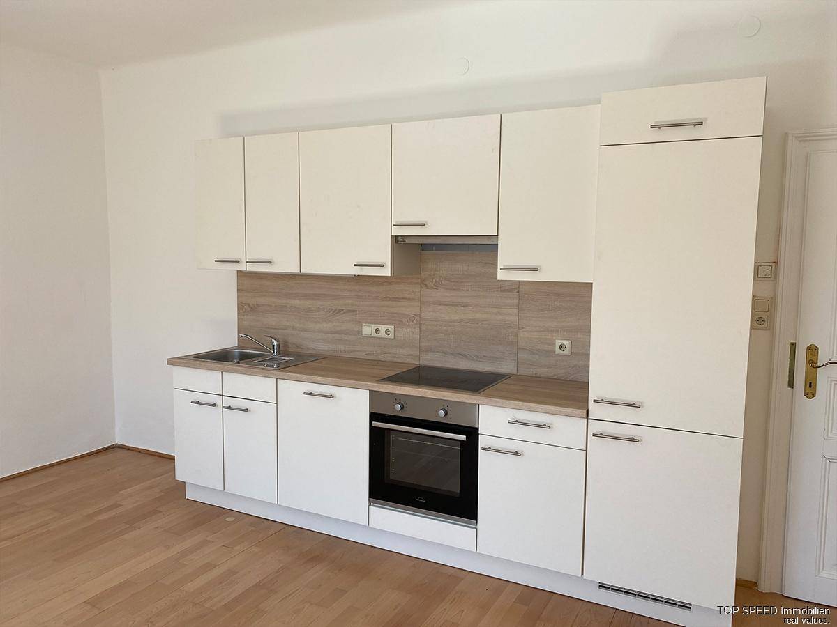 Nahaufnahme der modernen Küchenzeile mit weißen Schränken, Backofen und Kochfeld.