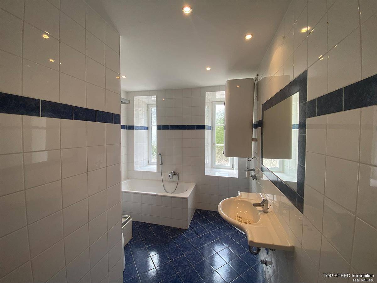 Badezimmer mit blauen und weißen Fliesen, Badewanne und Waschbecken, ausgestattet mit Spiegelschrank.