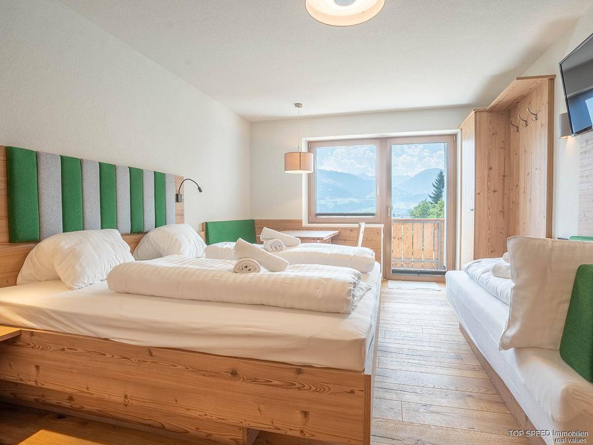 Helles Schlafzimmer mit Holzboden, Doppelbett und Zugang zu einem Balkon mit Bergblick.