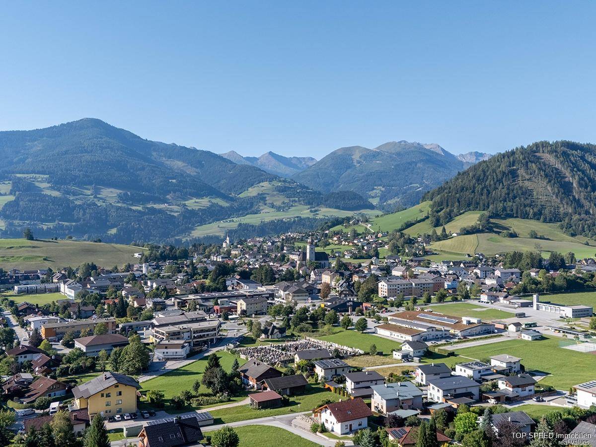 Weitläufiger Blick über eine charmante Stadt in einem grünen Tal, umgeben von Bergen.