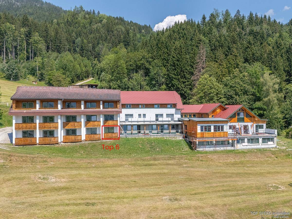Gebäudekomplex in alpiner Umgebung mit markierter Einheit "Top 6" und umgebender Natur.