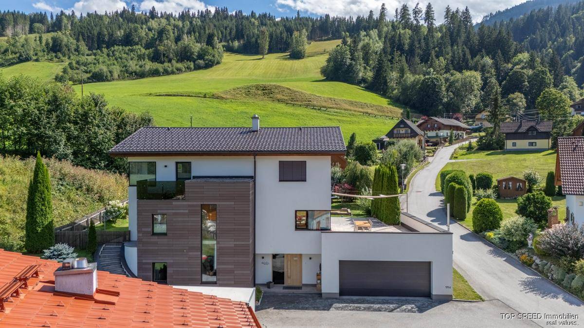 Moderne Hausfassade mit integrierter Garage und einer sonnigen Dachterrasse mit Blick ins Grüne.