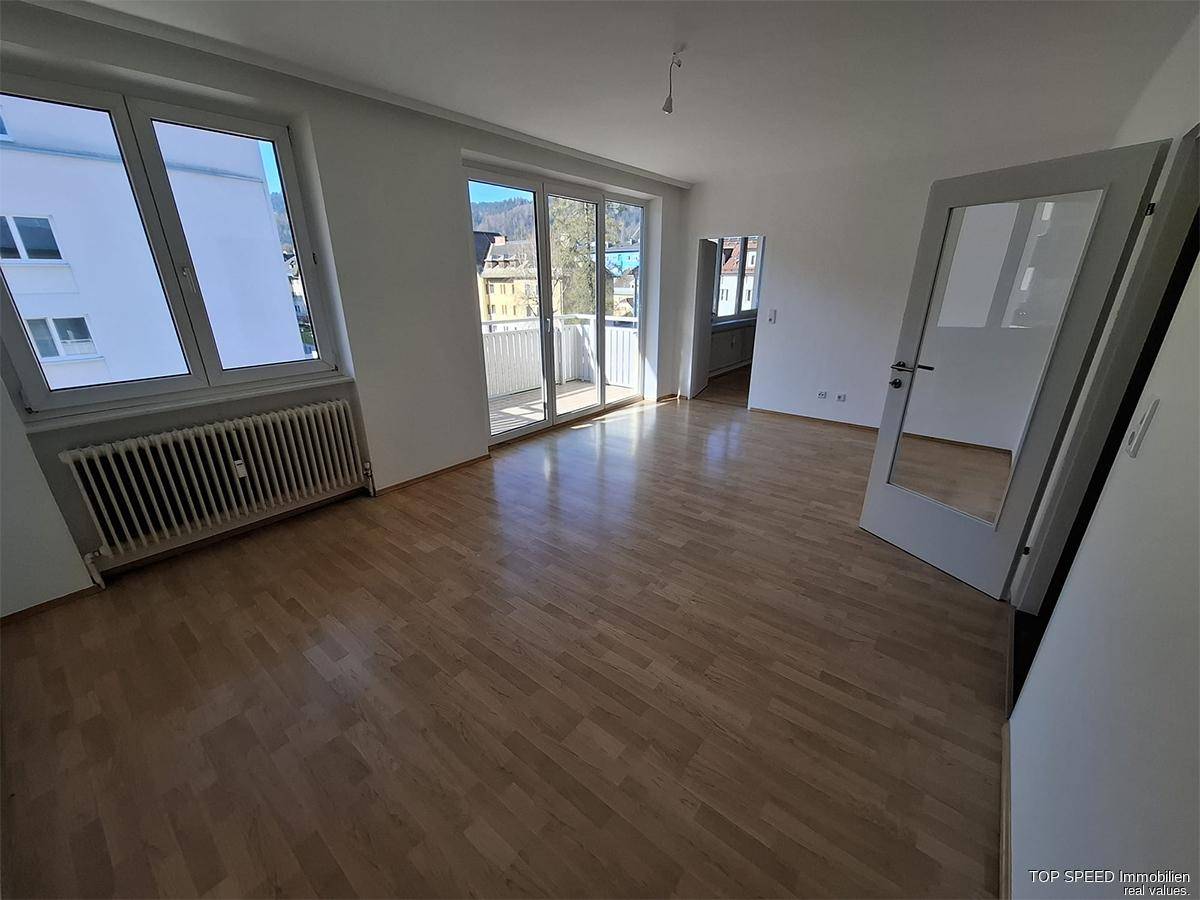 Geräumiges Wohnzimmer mit Parkettboden, großen Fenstern und Zugang zum Balkon.