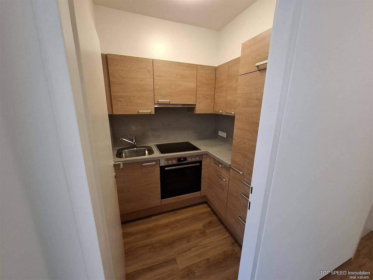Kompakte Einbauküche mit Holzfronten, Induktionskochfeld und integriertem Backofen.