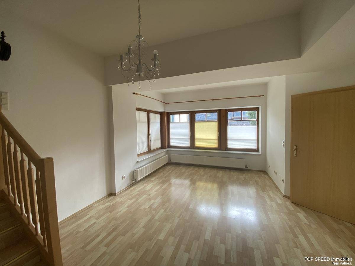 Geräumiges Wohnzimmer mit Laminatboden, Erkerfenstern und einem eleganten Kronleuchter.