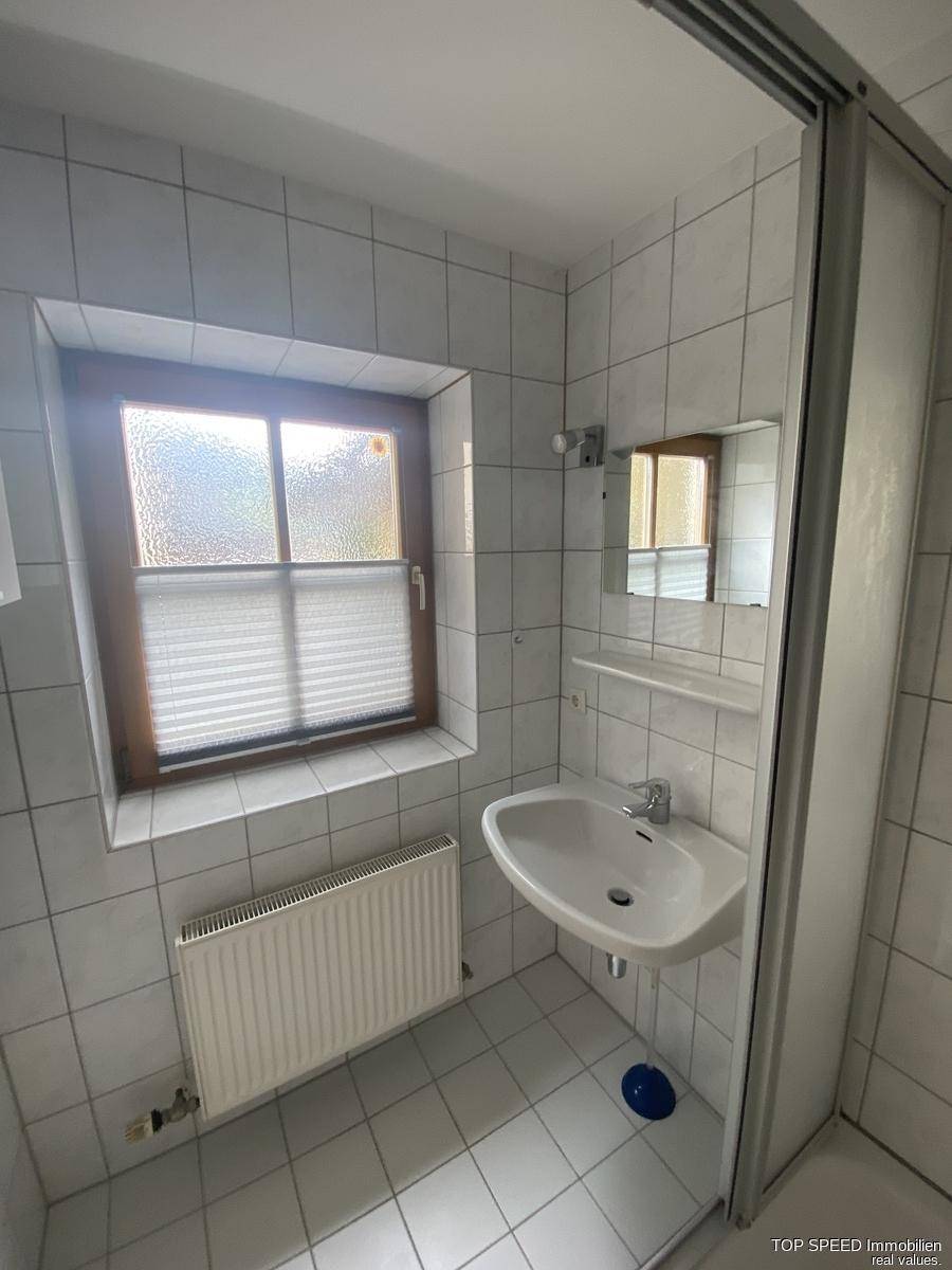 Funktionales Badezimmer mit Dusche, Waschbecken und Fenster in hellen Fliesen.