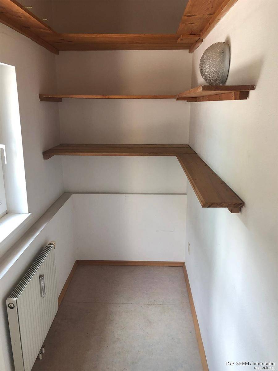 Praktischer Abstellraum mit Holzregalen, Heizkörper und Fenster für Tageslicht.