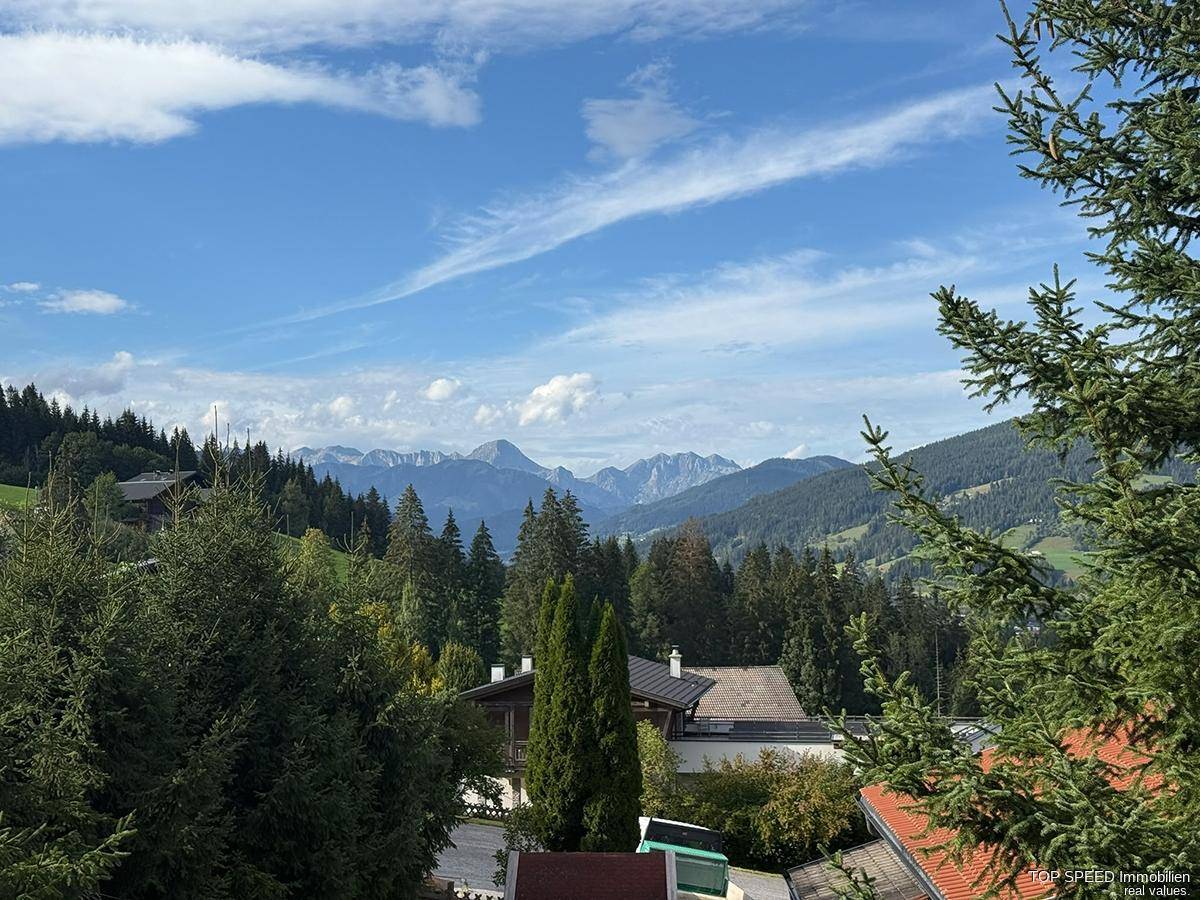 Panoramablick auf die majestätischen Berge und grüne Wälder unter einem weiten blauen Himmel.