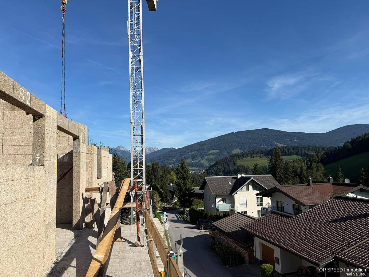 Blick von der Baustelle eines Neubaus auf die umliegende Berglandschaft und andere Häuser.