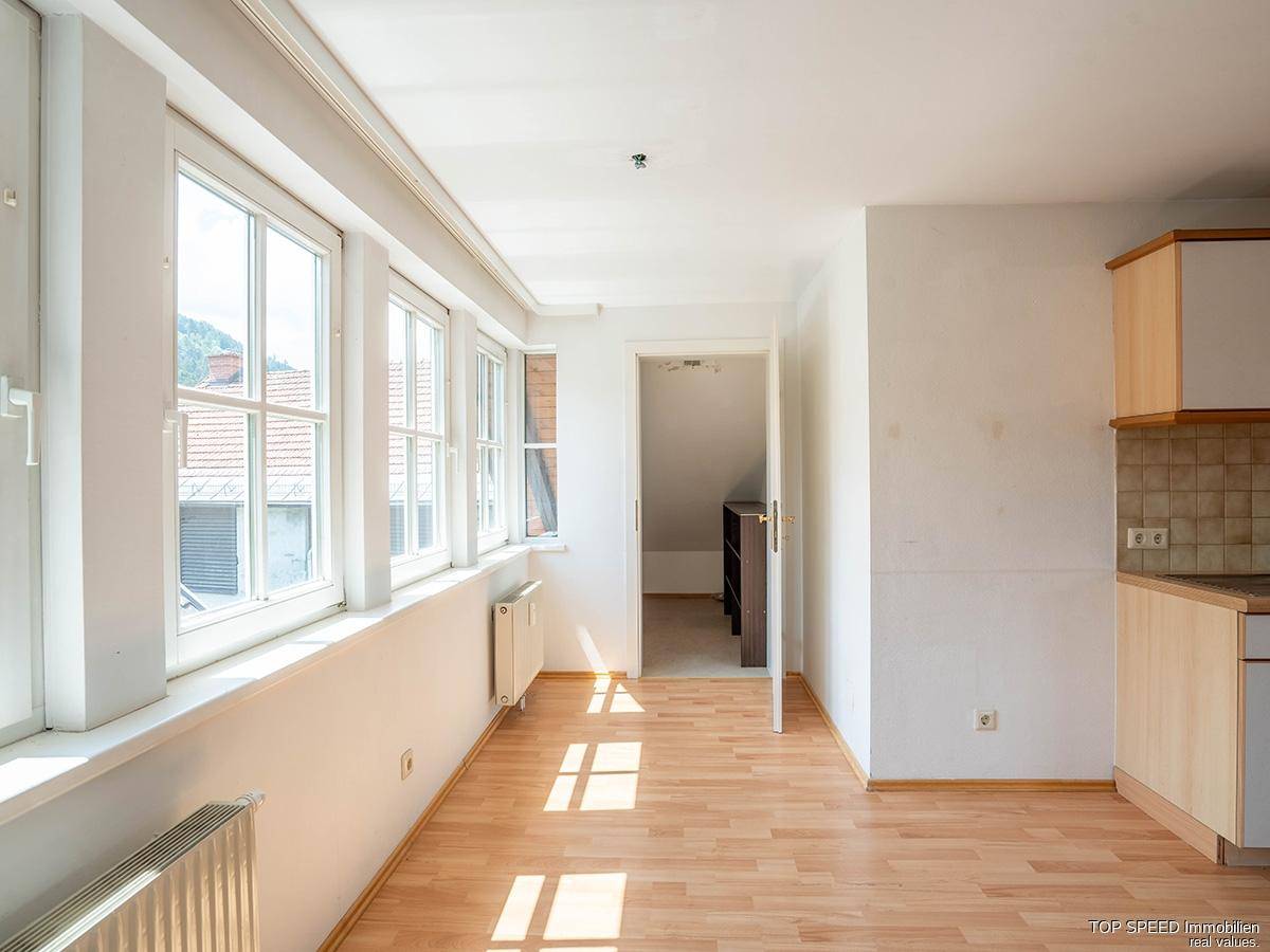 Lichtdurchfluteter Wohnbereich mit großen Fenstern, Laminatboden und Zugang zu einem weiteren Zimmer.