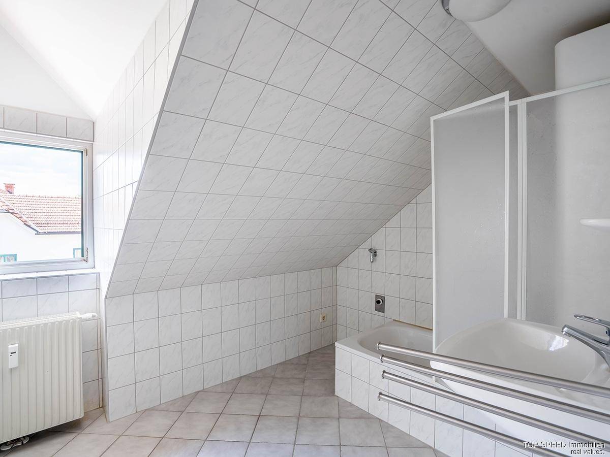 Gefliestes Badezimmer im Dachgeschoss mit Badewanne, Dusche und Fenster.