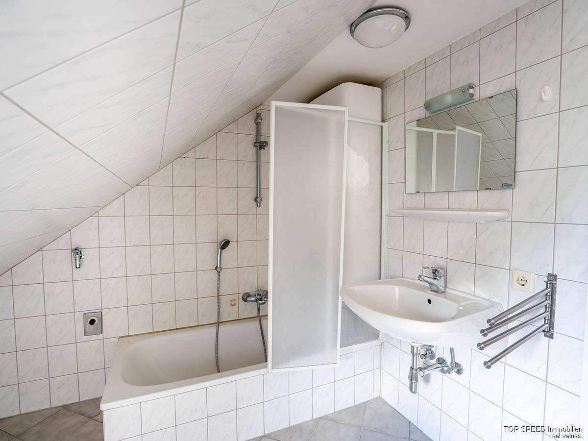 Helles Badezimmer mit Badewanne, Duschabtrennung, Waschbecken und Wandspiegel.