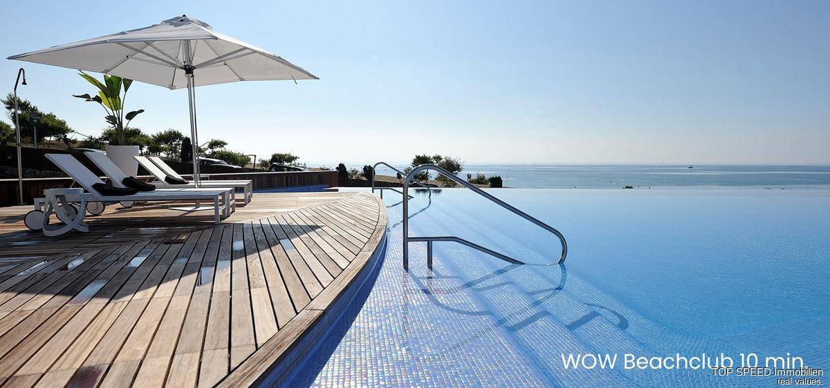 Infinity-Pool mit Holzdeck und Sonnenliegen, bietet einen atemberaubenden Blick auf das Meer.