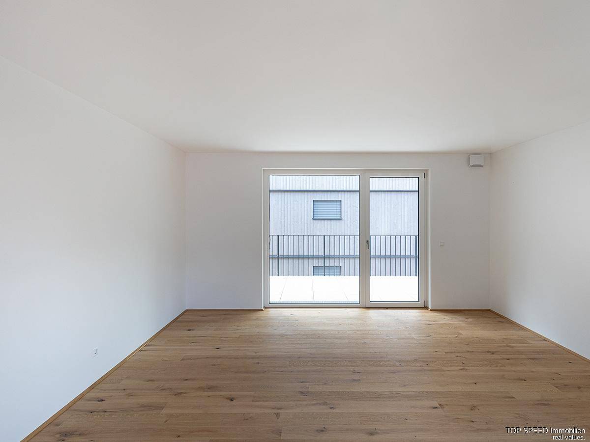 Heller Raum mit Holzboden und großer Schiebetür, die zu einem Balkon führt.