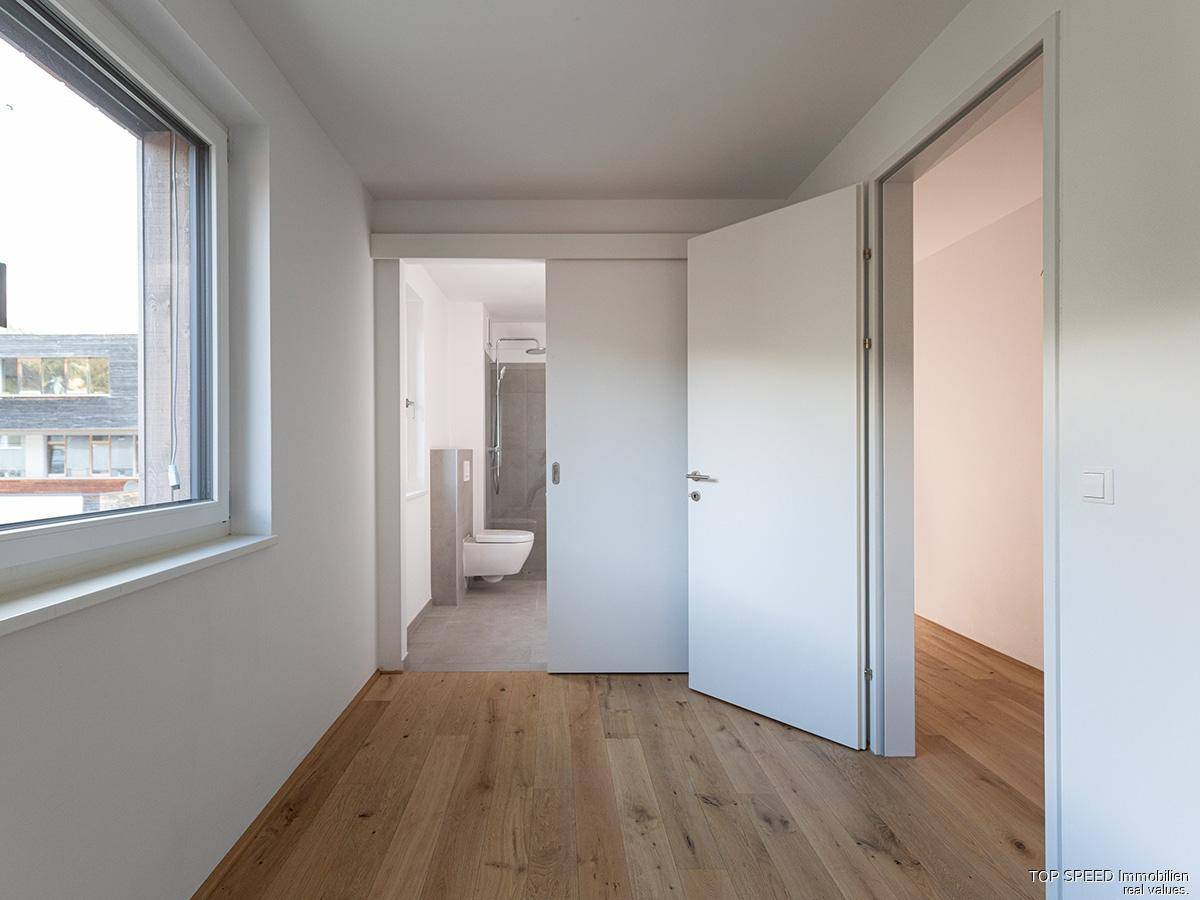 Schlafzimmer mit Holzboden und Zugang zu einem modernen Badezimmer mit Dusche.