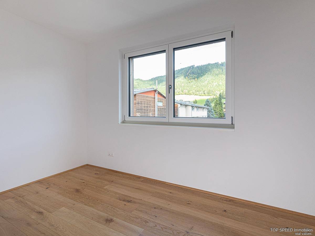 Freundliches Schlafzimmer mit Holzboden und Fensterblick auf die Berge.