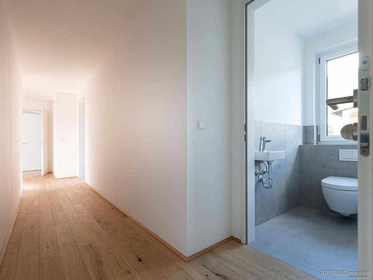 Heller Flur mit Holzboden und Blick in ein modernes Gäste-WC mit Fenster.
