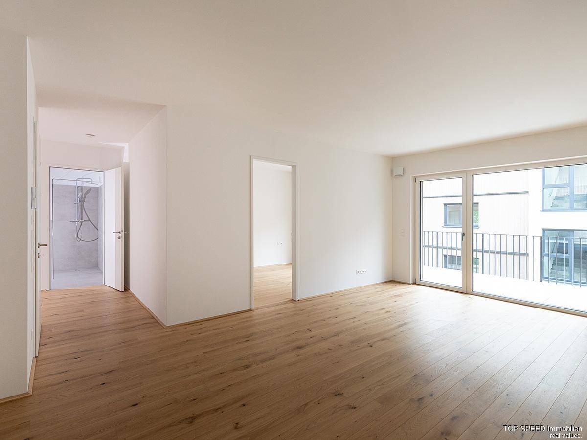 Heller, leerer Wohnraum mit Eichenparkettboden und großem Schiebefenster zum Balkon.