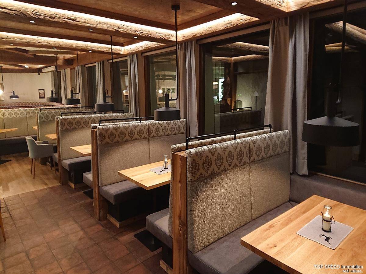 Gemütlicher Restaurantbereich mit Holzbalken, gepolsterten Sitzbänken und großen Fenstern.
