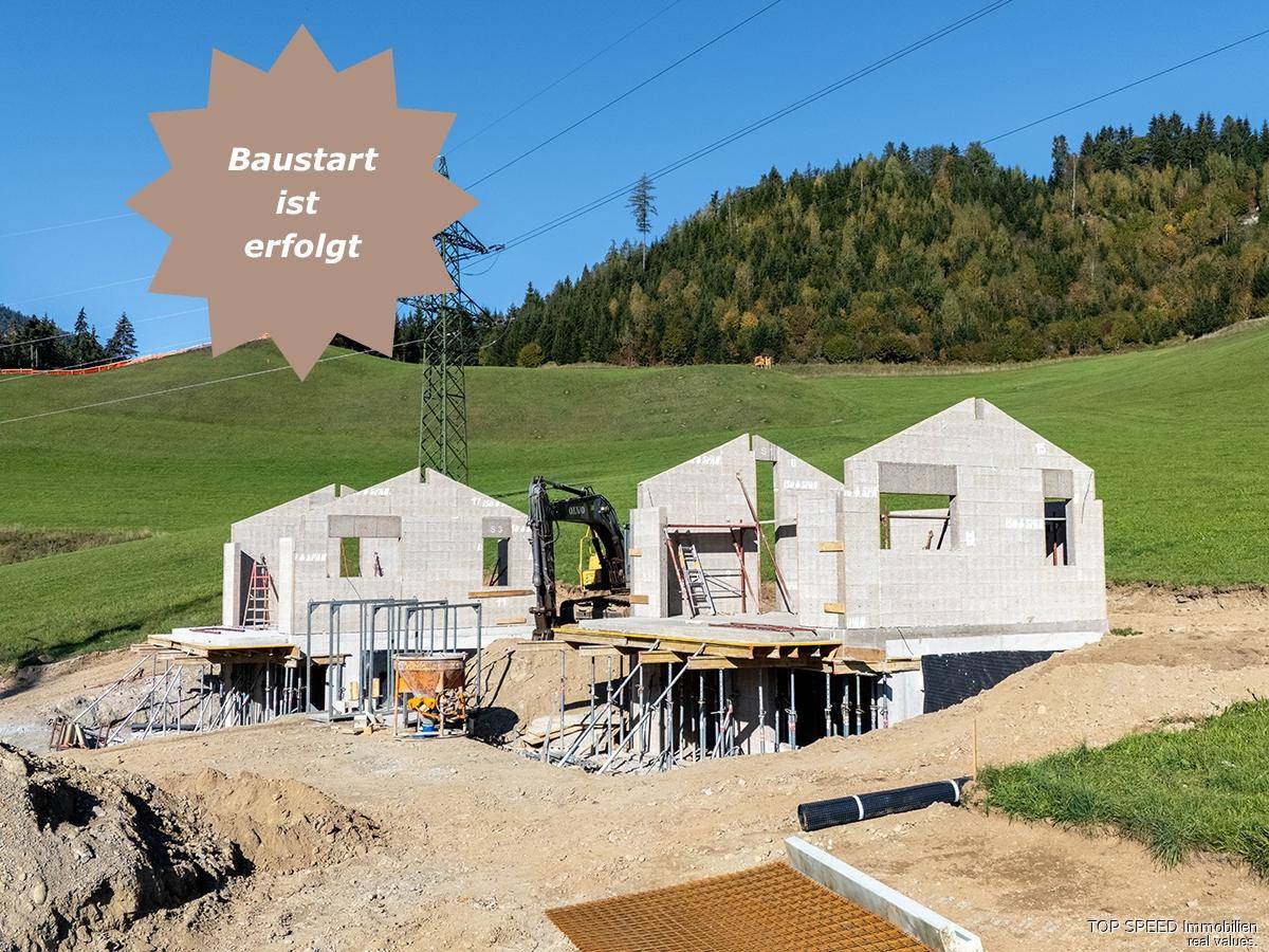 Baustelle mit im Bau befindlichen Häusern in einer grünen Hügellandschaft, der Baustart ist erfolgt.