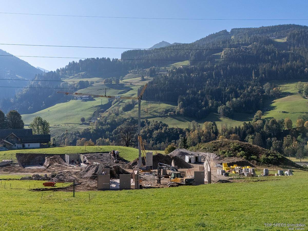 Panoramablick auf eine Baustelle in einem grünen Tal, umgeben von bewaldeten Hügeln und Bergen.