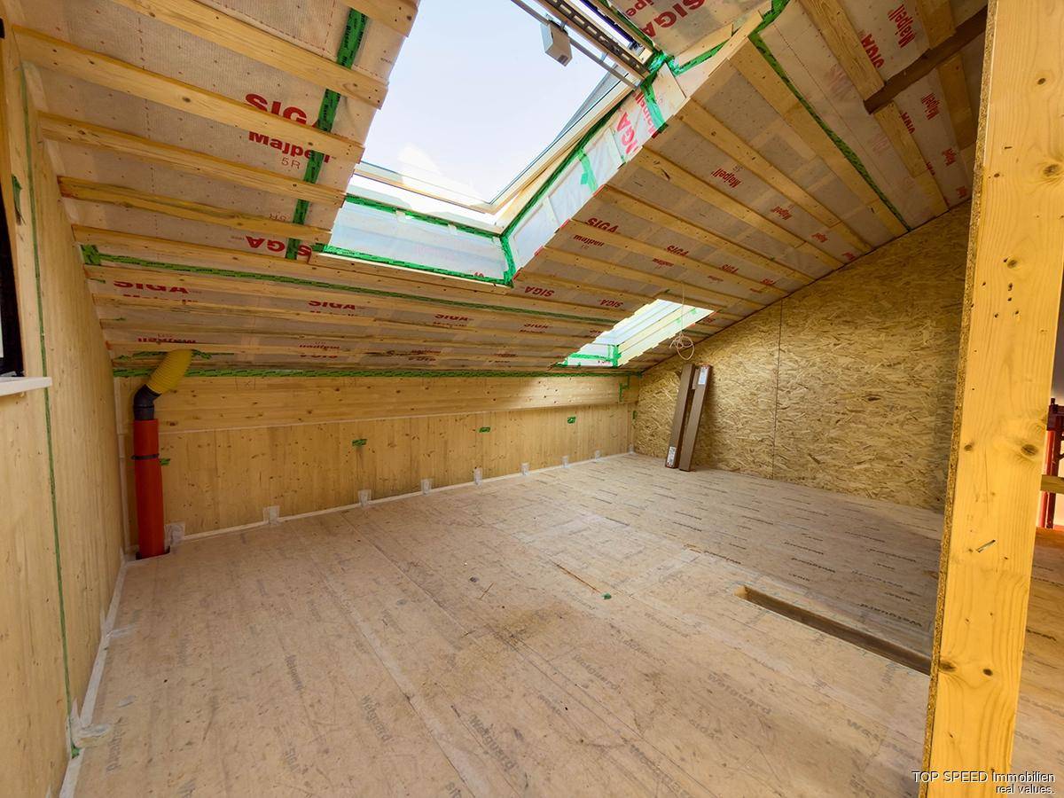 Unfertiger Innenraum im Dachgeschoss mit Holzverkleidung, Dachschrägen und Oberlichtern.
