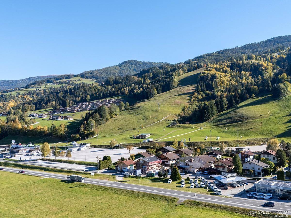 Weitläufige Ansicht der Ortschaft mit grünen Hängen und Skipisten im Herbst.