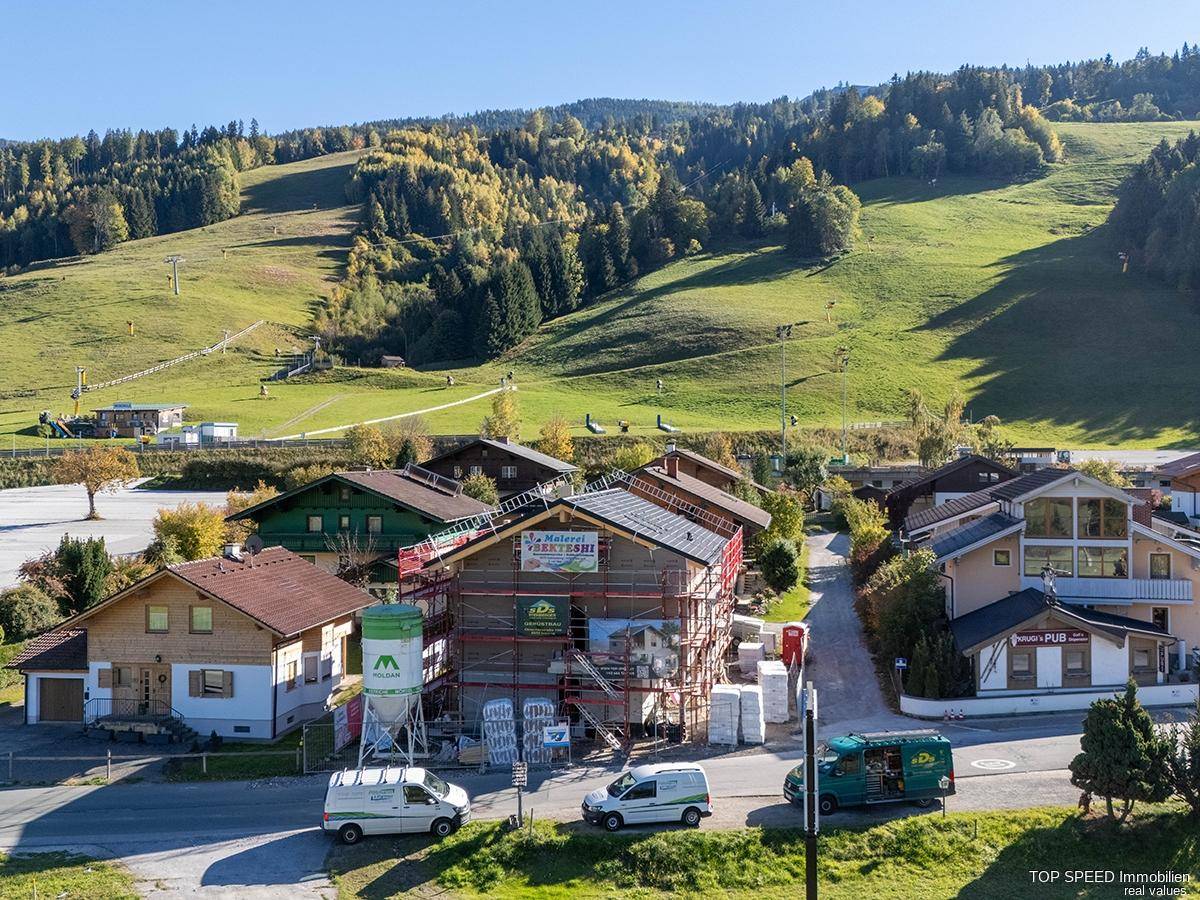 Überblick über den Neubau mit Gerüst, umgeben von Häusern und grünen Bergen.