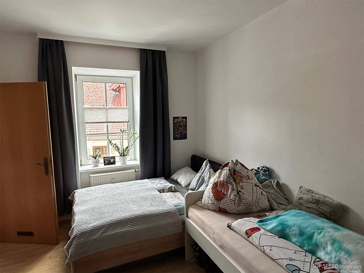 Schlafzimmer mit zwei Einzelbetten, dunklen Vorhängen und hellem Holzfußboden.