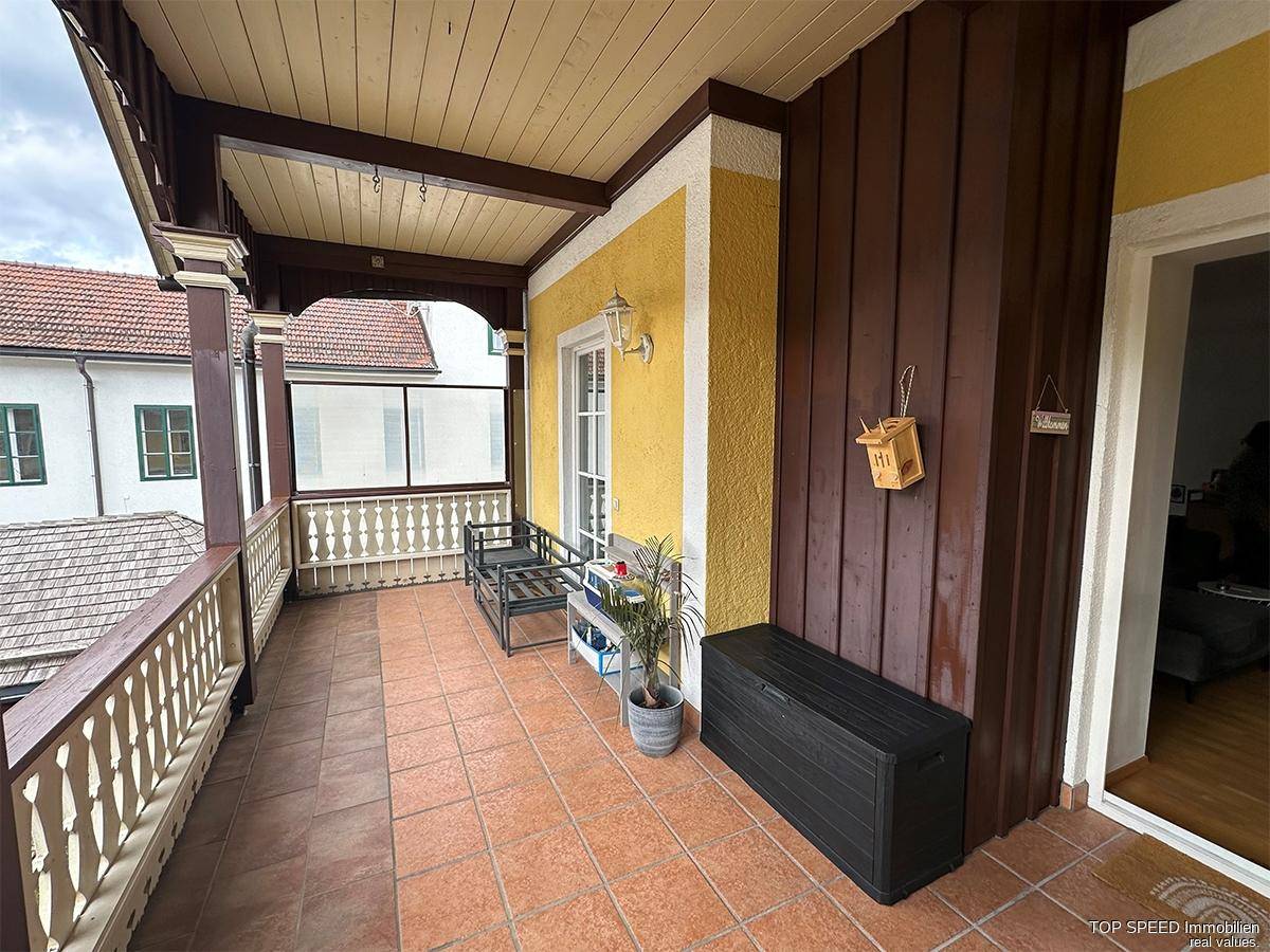 Überdachter Balkon mit Holzboden und -geländer, gefliestem Boden und Sitzgelegenheiten.