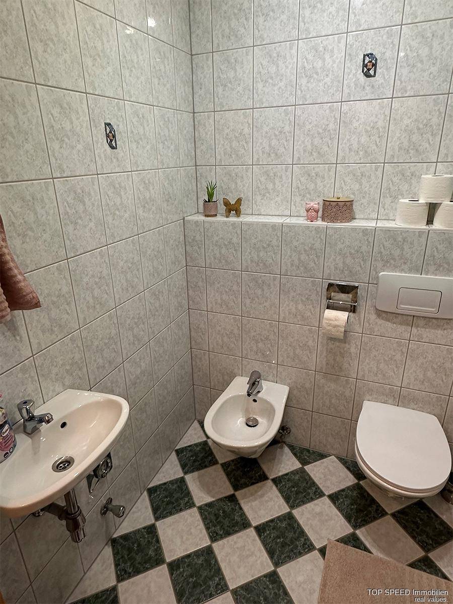 Separates WC mit Bidet, kleinem Waschbecken und auffälligem Schachbrettmuster auf dem Boden.
